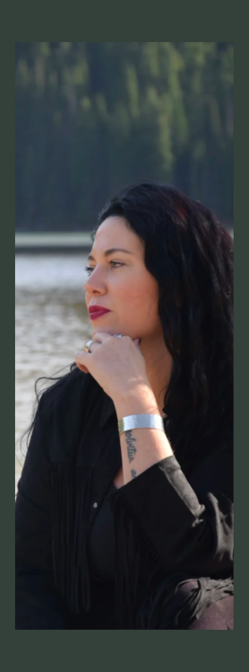 Woman with dark hair and a black top sitting by a body of water with trees in the background
